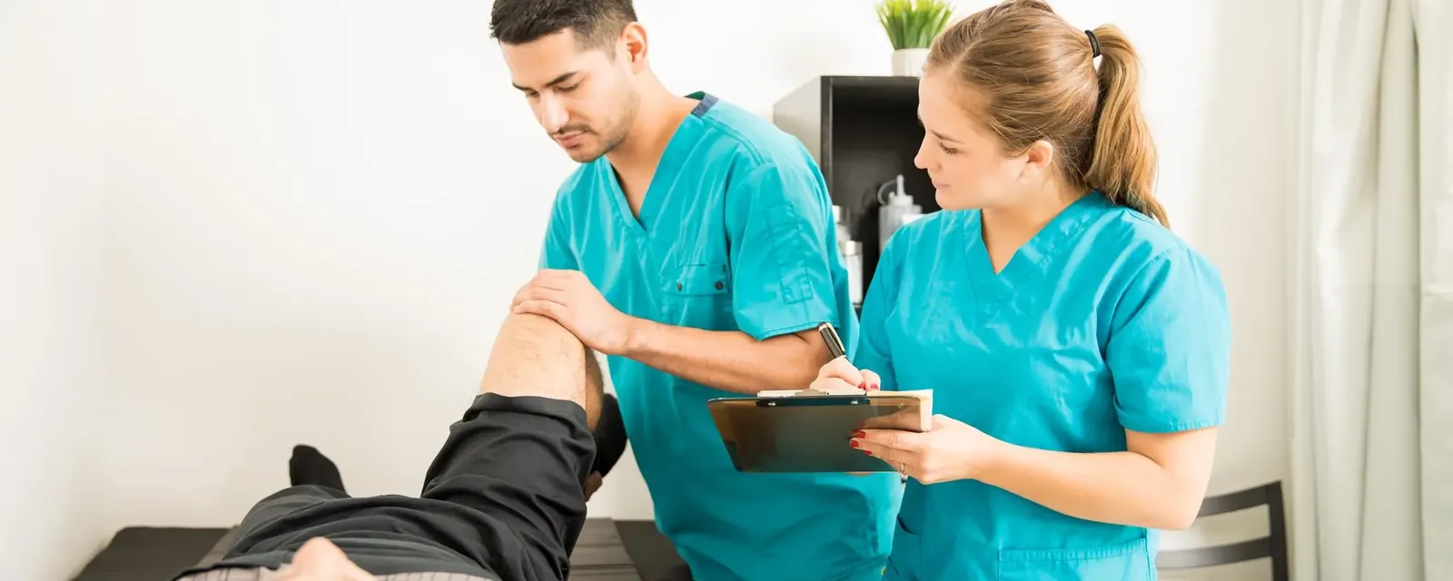 Two allied health practitioners assessing a patient on a treatment table using a tablet