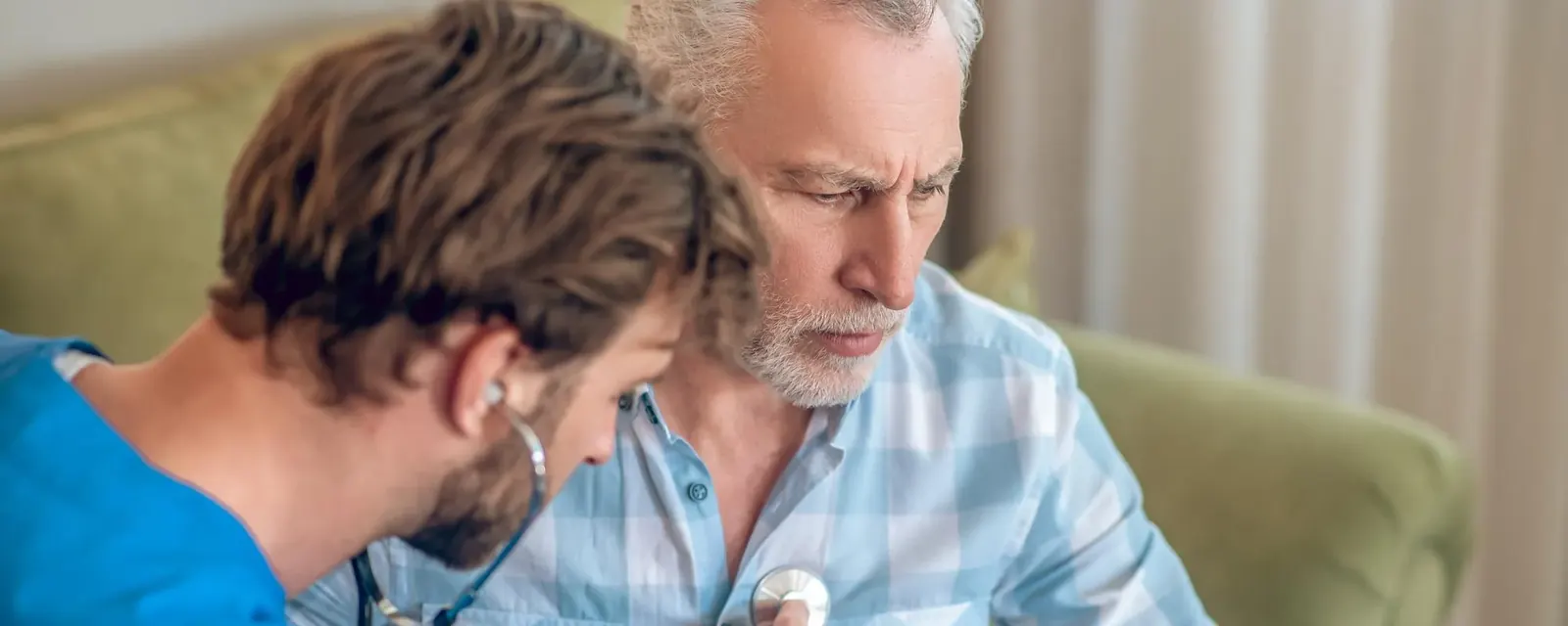 A general practitioner listening to an older patient's chest with a stethoscope during a consultation