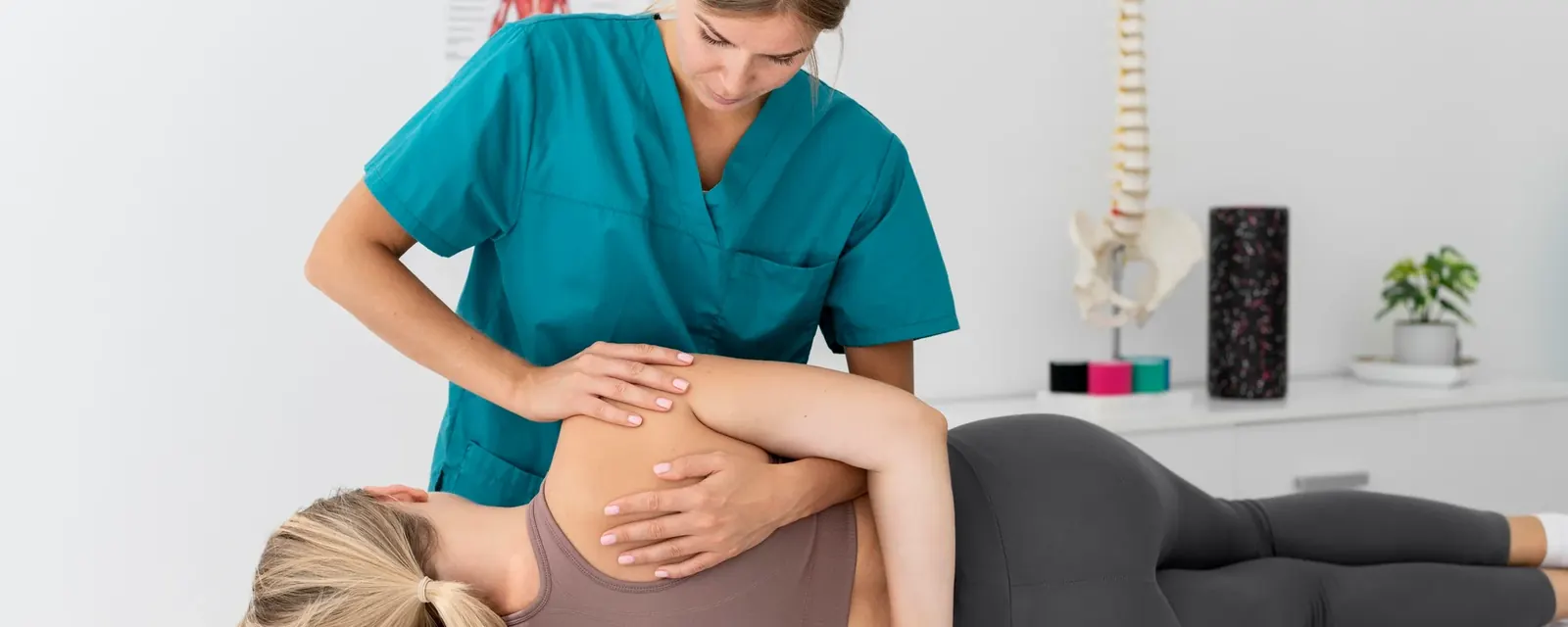 A physiotherapist treating a patient's lower back on a treatment table beside a spine model
