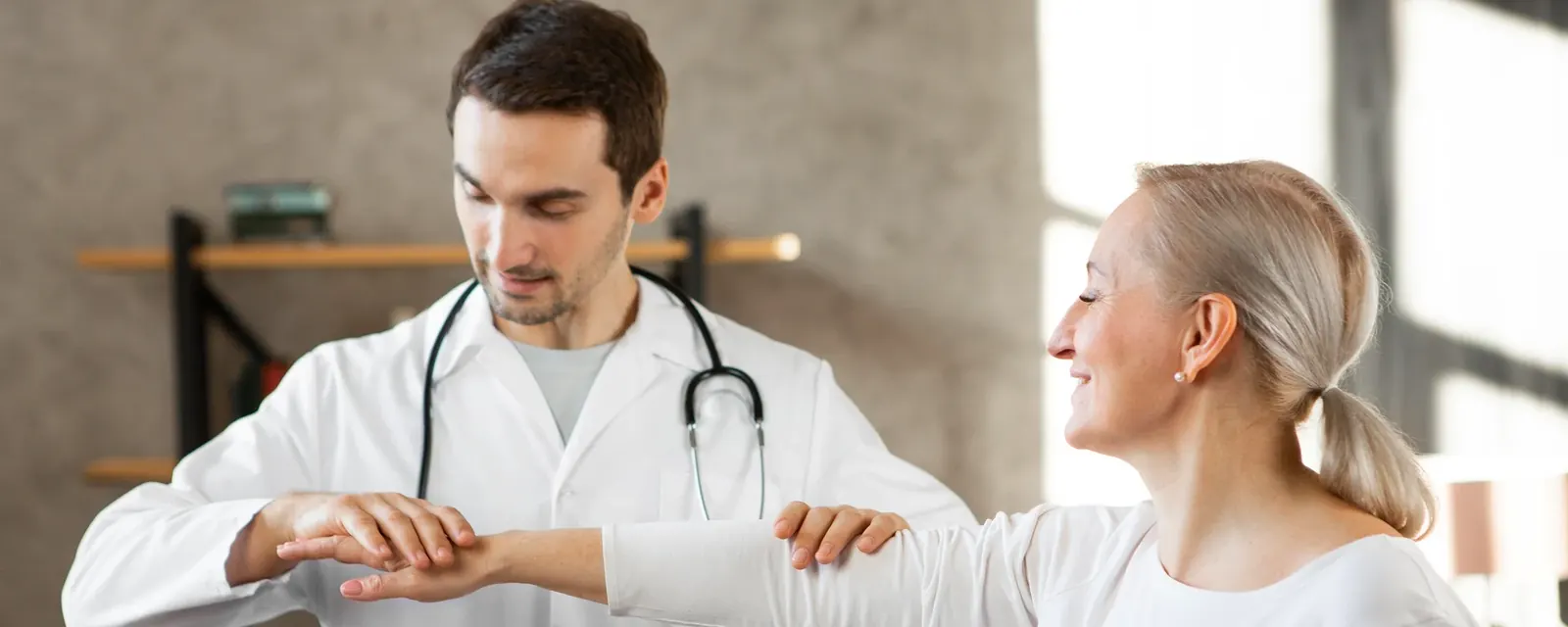 A practitioner assessing a patient's arm and shoulder movement in a consulting room